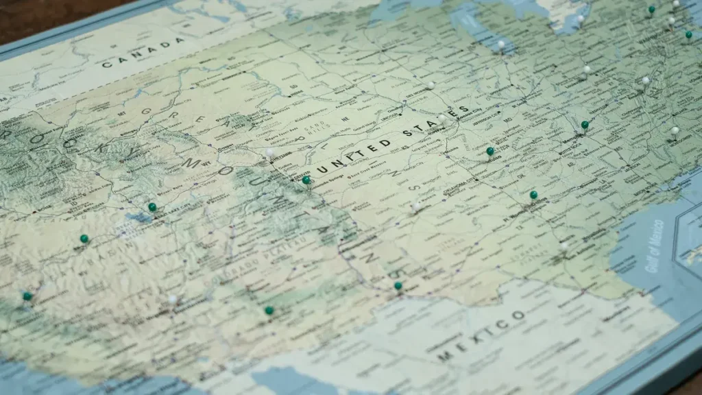 Map of the United States with push pins in several states, on a wooden desk